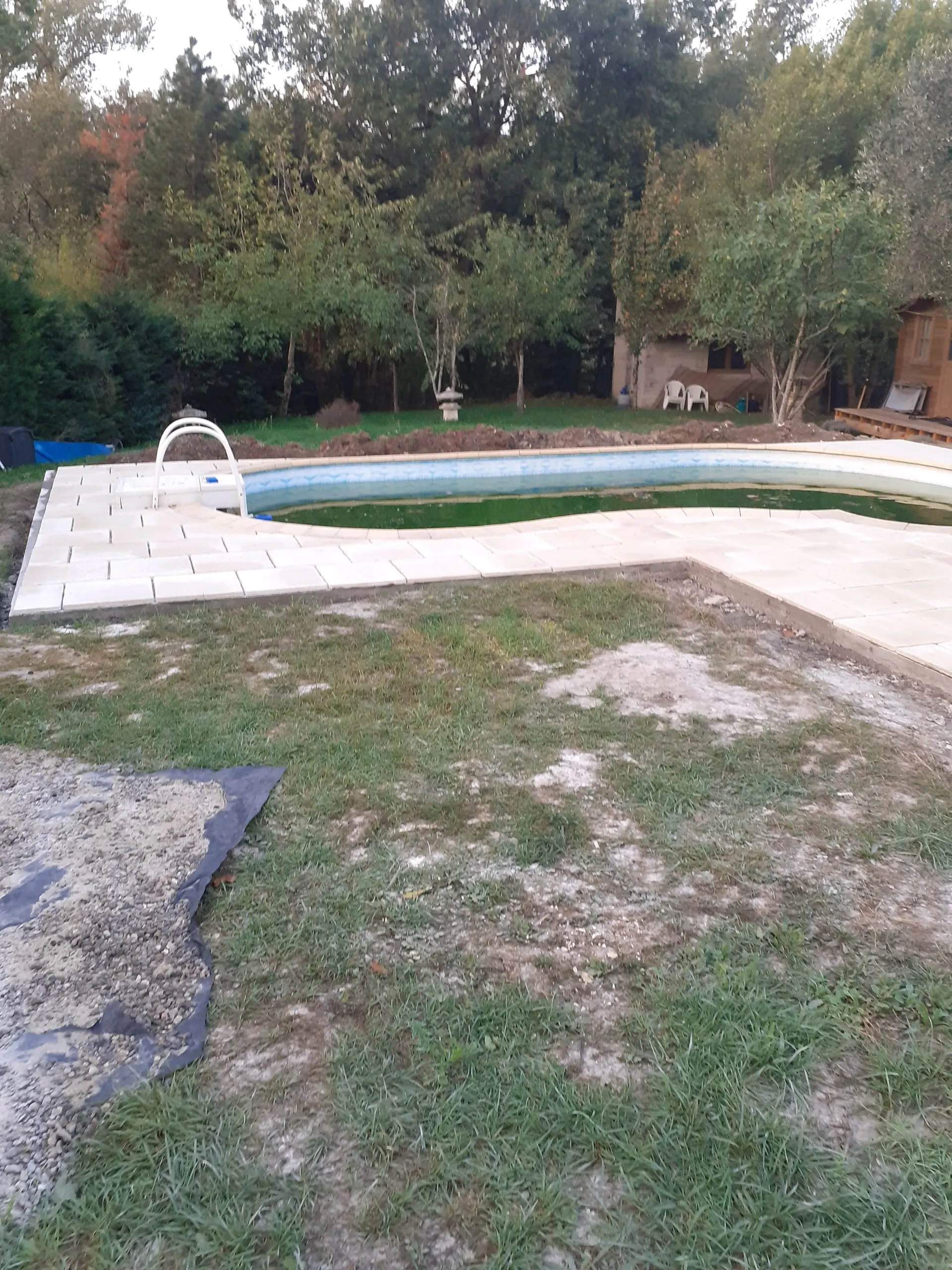 Dallage clair posé autour d’une piscine dans un jardin arboré.