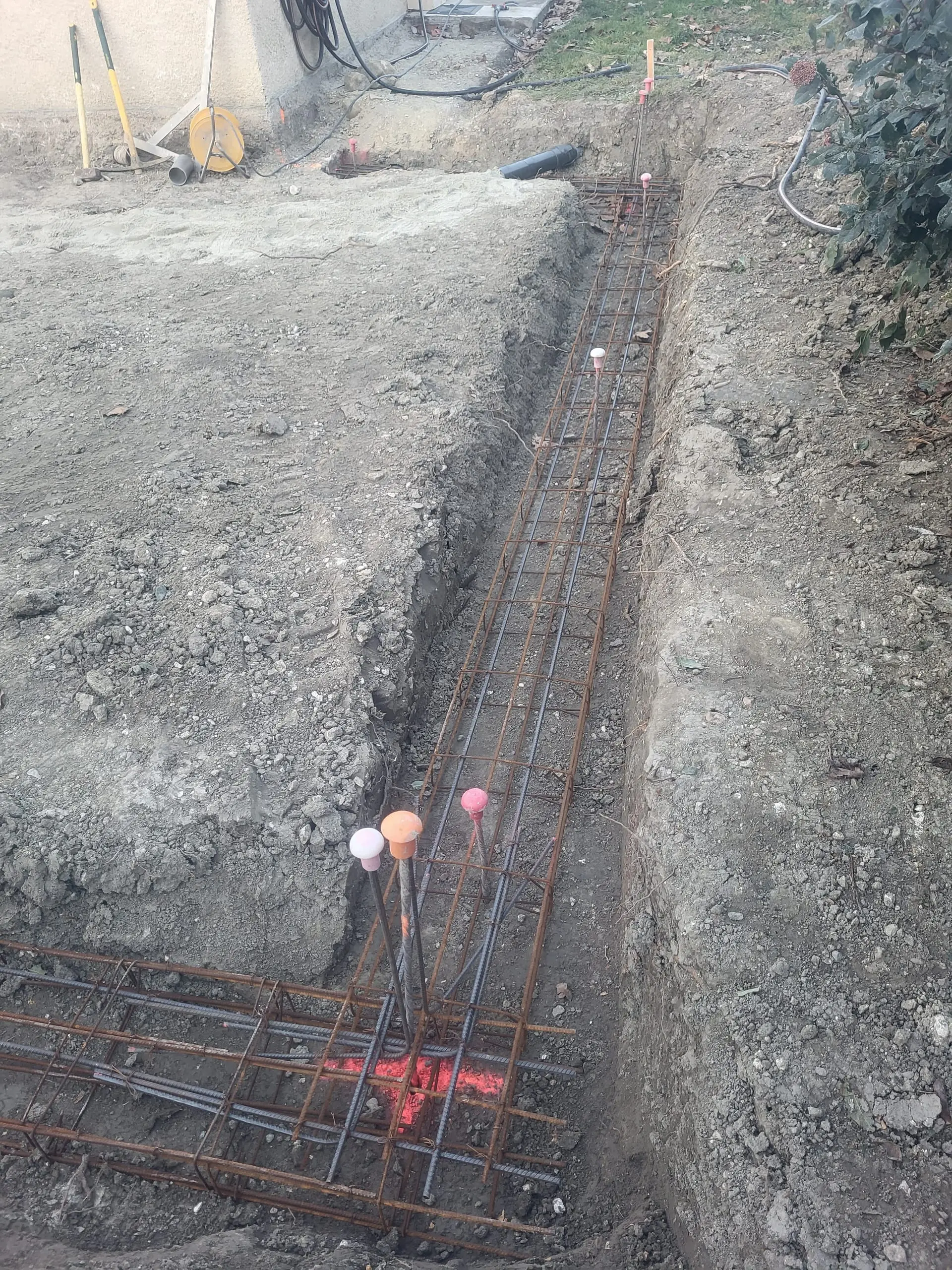 Ferraillage de fondations disposé dans une tranchée au pied d’une maison.