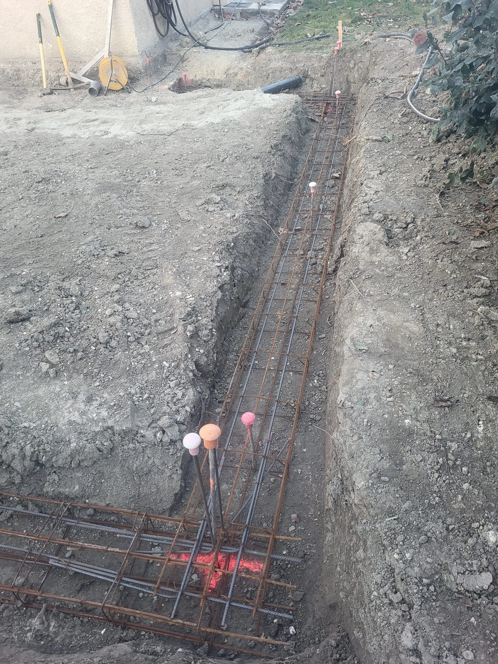 Ferraillage de fondations disposé dans une tranchée au pied d’une maison.
