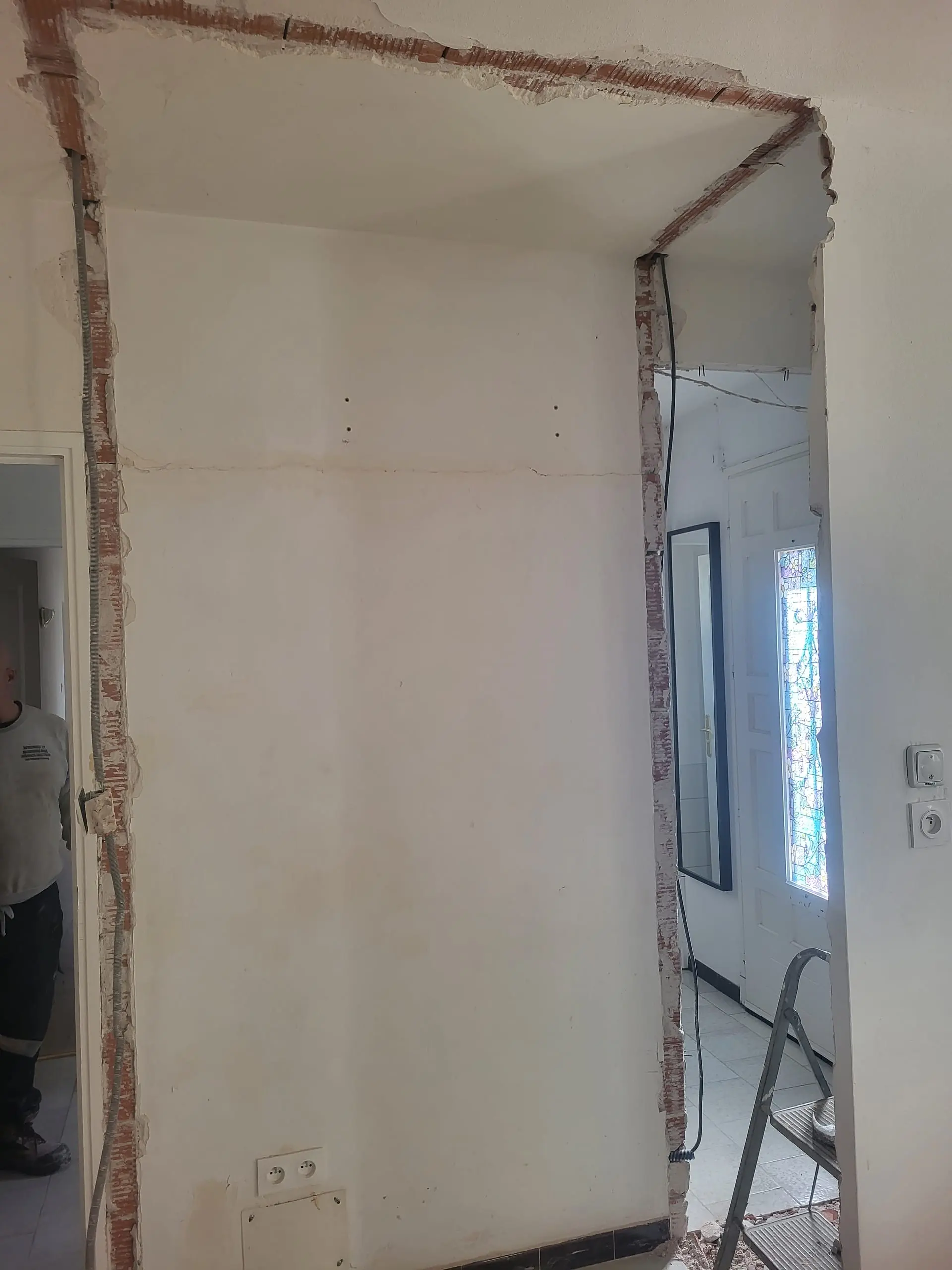 Création d’une grande ouverture dans une cloison en briques pendant une rénovation intérieure.
