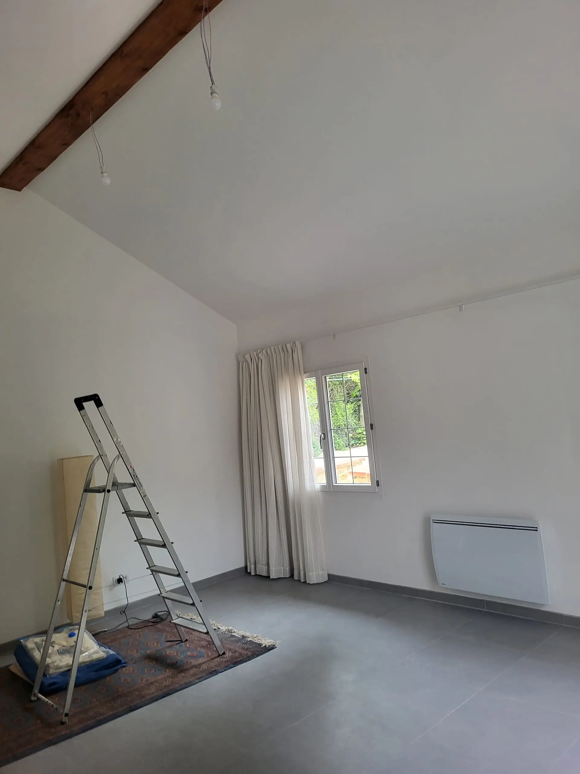 Pièce rénovée aux murs blancs avec poutre en bois apparente et carrelage gris.