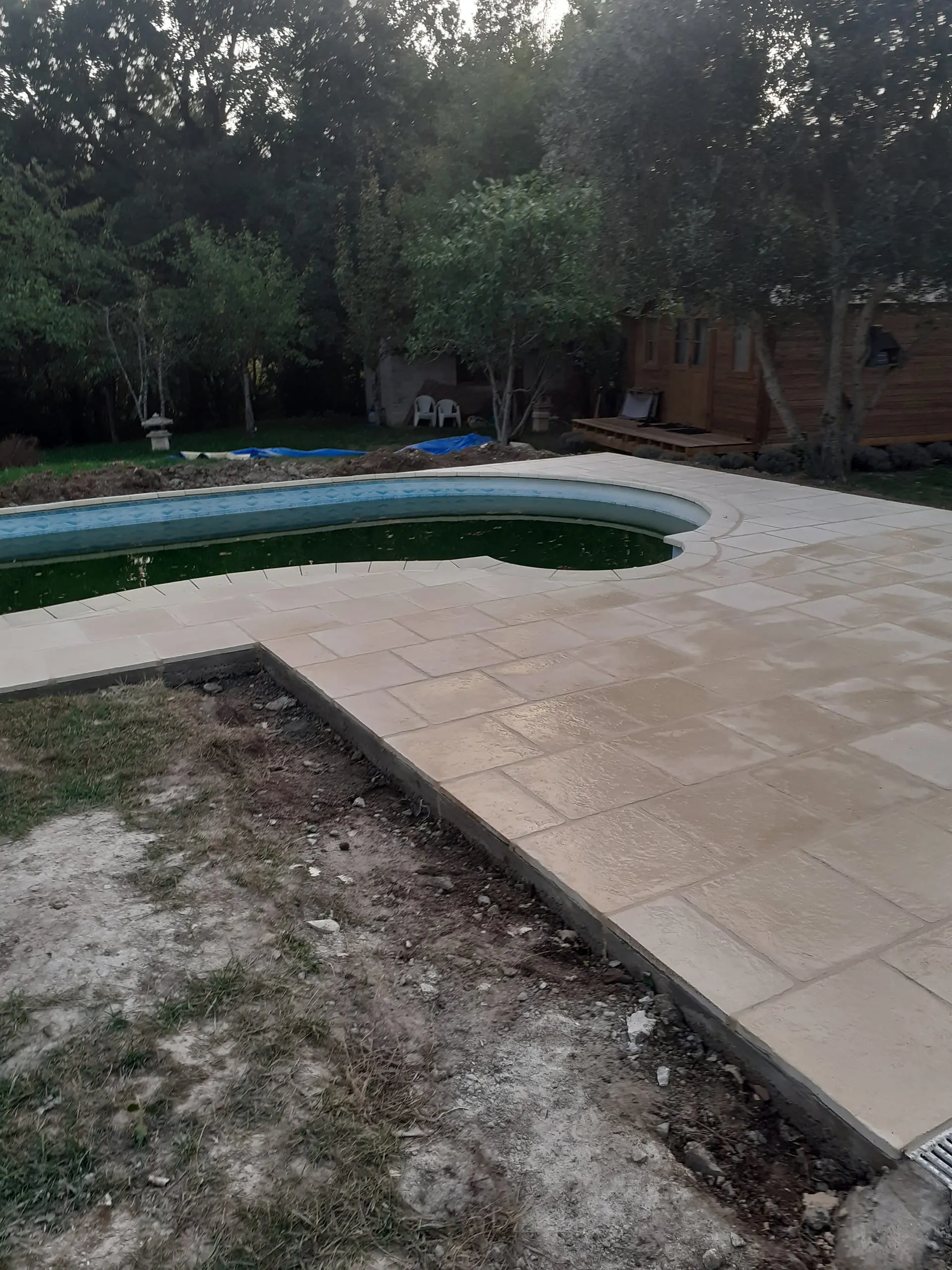 Dallage beige à motif pierre posé autour d’une piscine dans un jardin boisé.