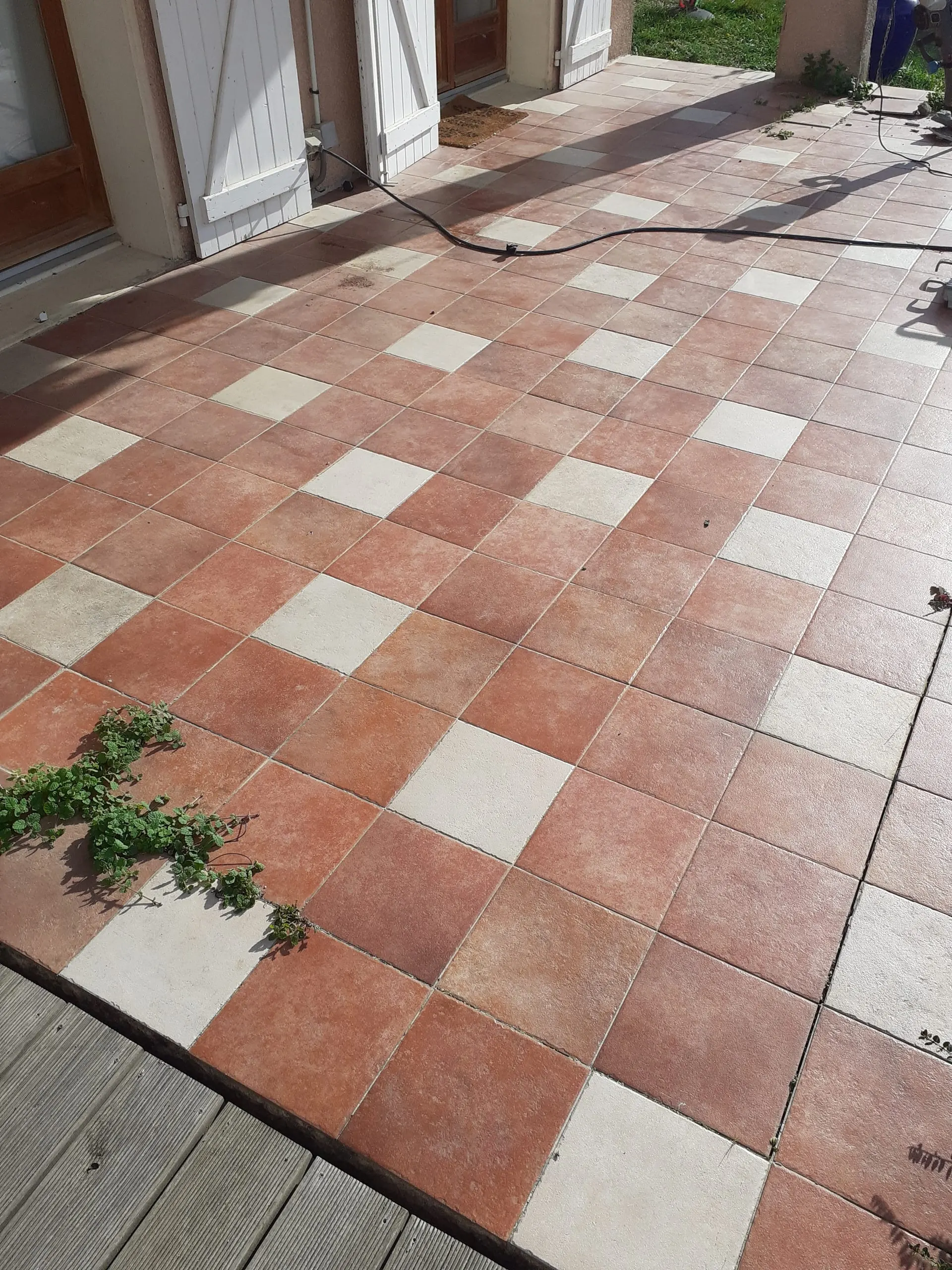 Terrasse extérieure carrelée de carreaux rouges et écrus devant une maison.